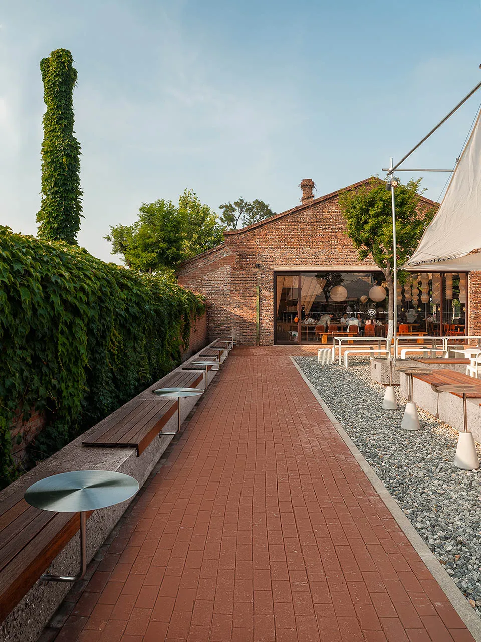 A brick walkway surrounded by dining tables, chairs, and benches in an inviting outdoor patio area