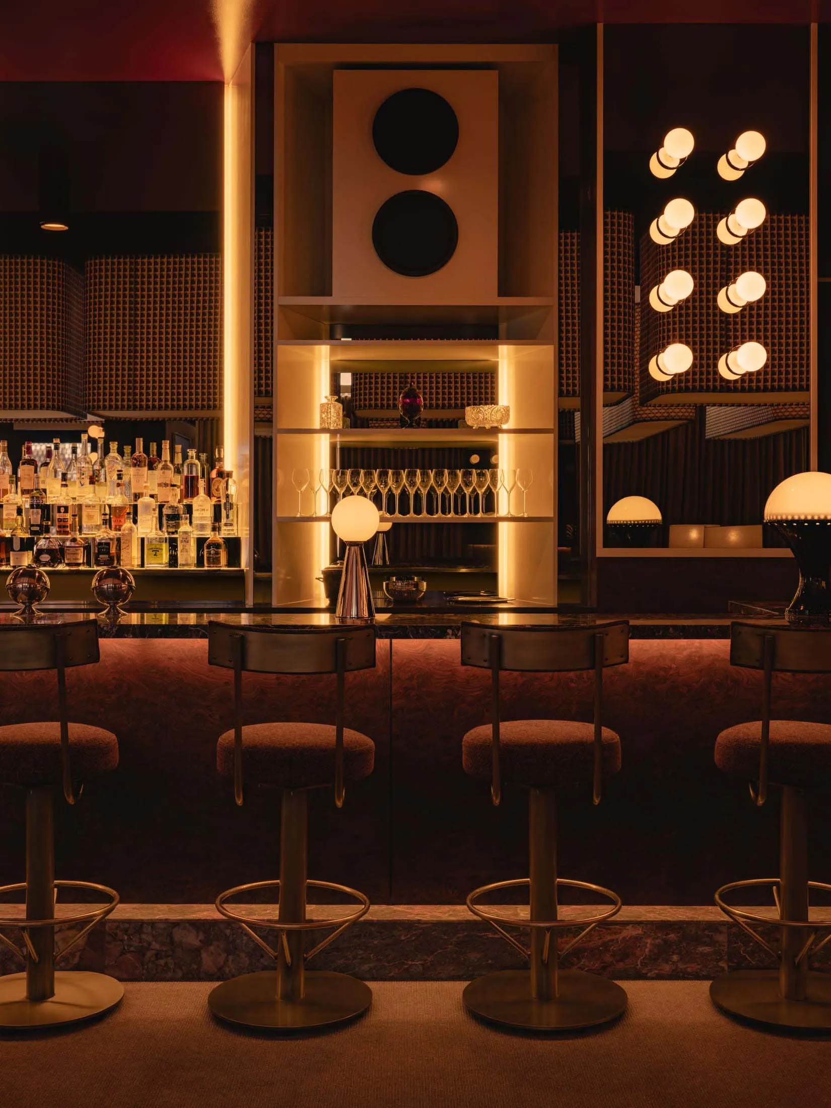 A sophisticated bar area with a long counter, stools, wine glasses, and bottles, set in a restaurant with a focus on comfort and dining experience