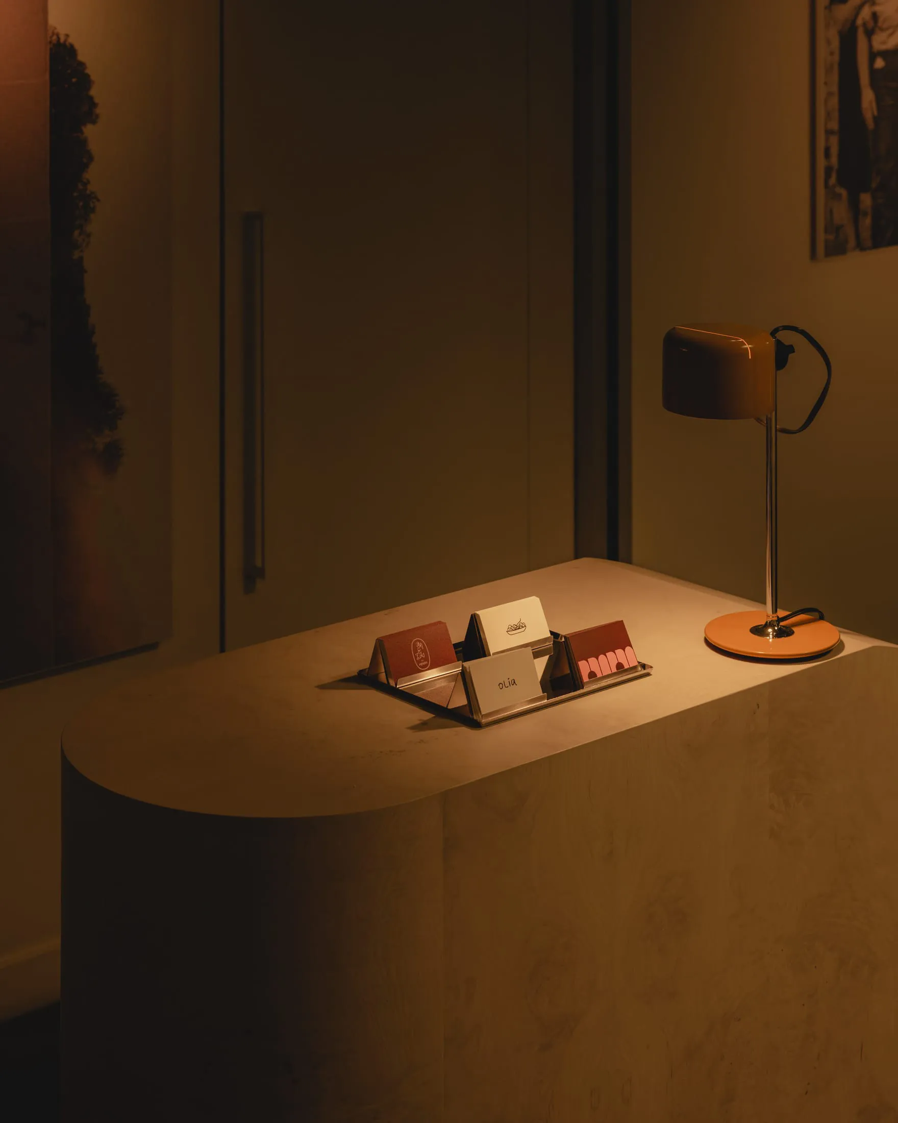A small, dimly lit room with a white desk, two books, and a lamp, creating a calm atmosphere