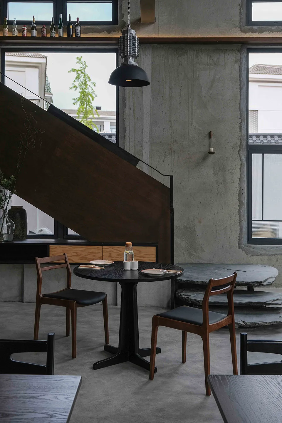 Modern restaurant interior with a black table, chairs, staircase, and potted plants