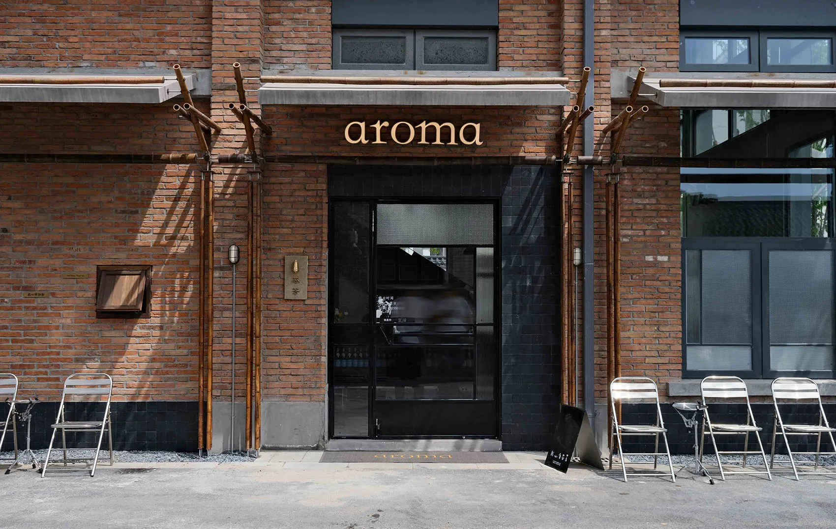 A welcoming restaurant entrance with a black doorway, glass windows, and outdoor seating area with a table and chairs