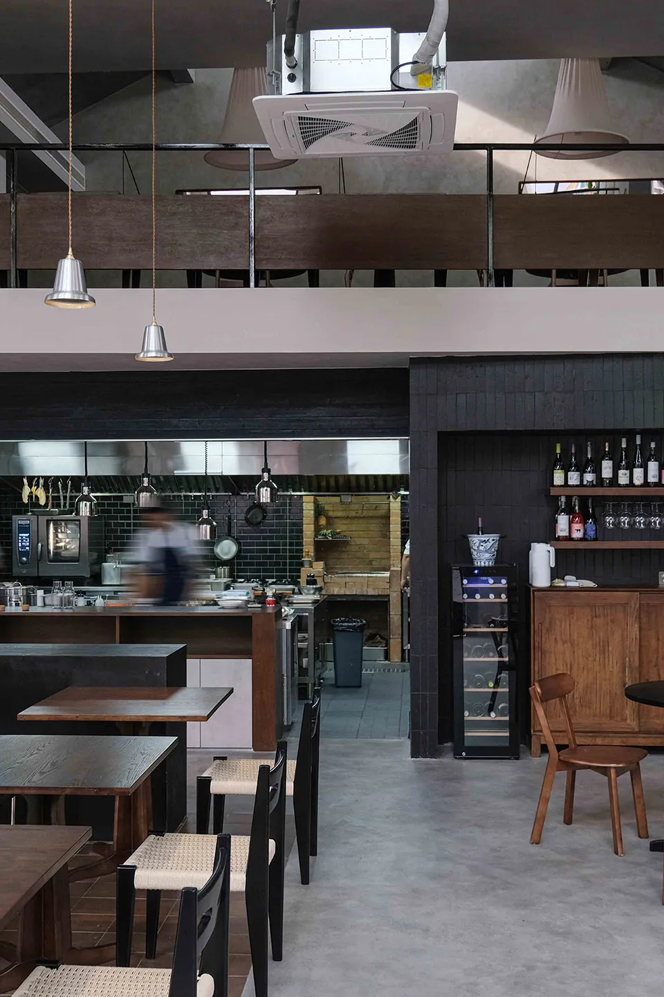 Modern restaurant interior with black walls, white elements, tables, chairs, kitchen appliances, and bottles of beverages