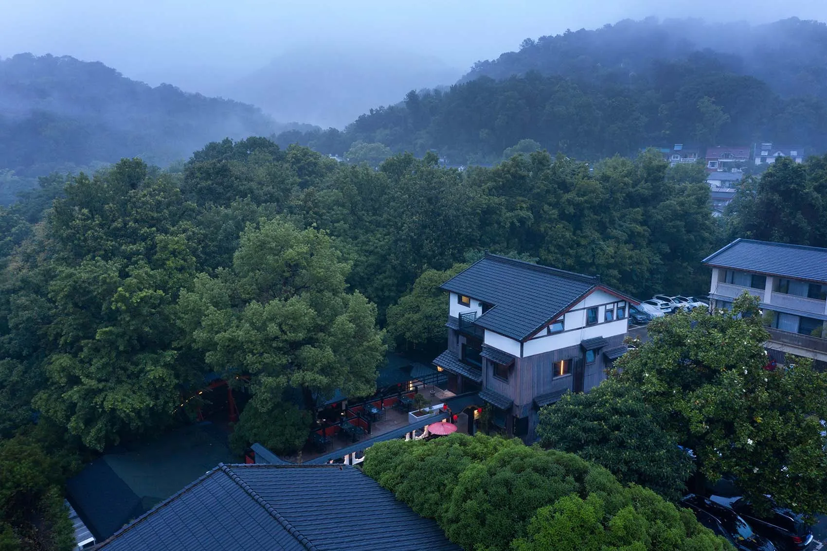 一座被森林環繞的房屋，擁有黑色屋頂與陽台，設有戶外座椅，營造寧靜氛圍