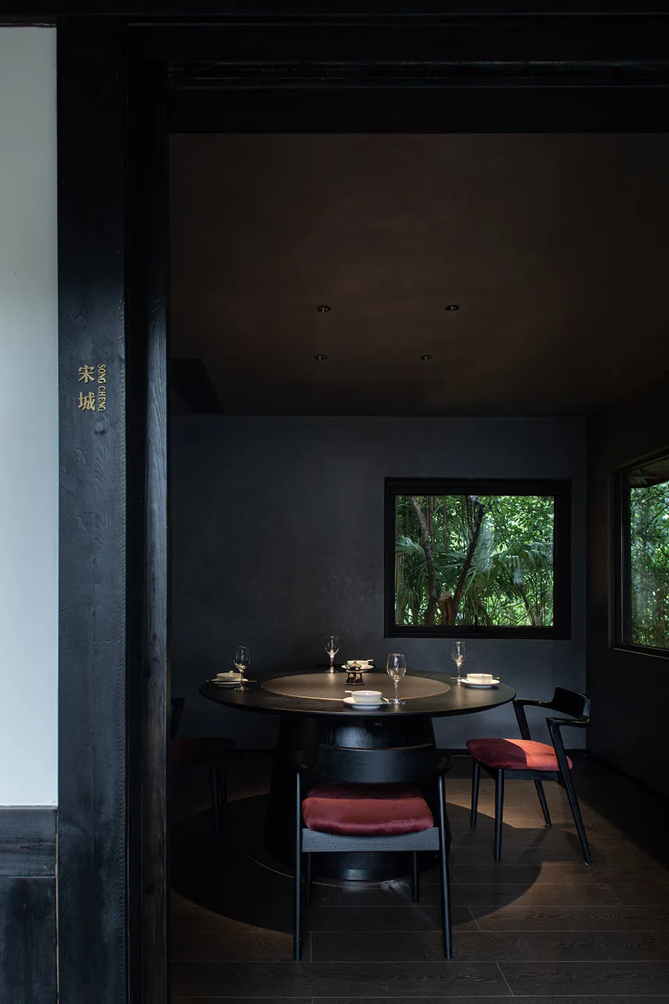 A modern dining area with a round table, chairs, wine glasses, bowls, and cups in a dimly lit Asian restaurant