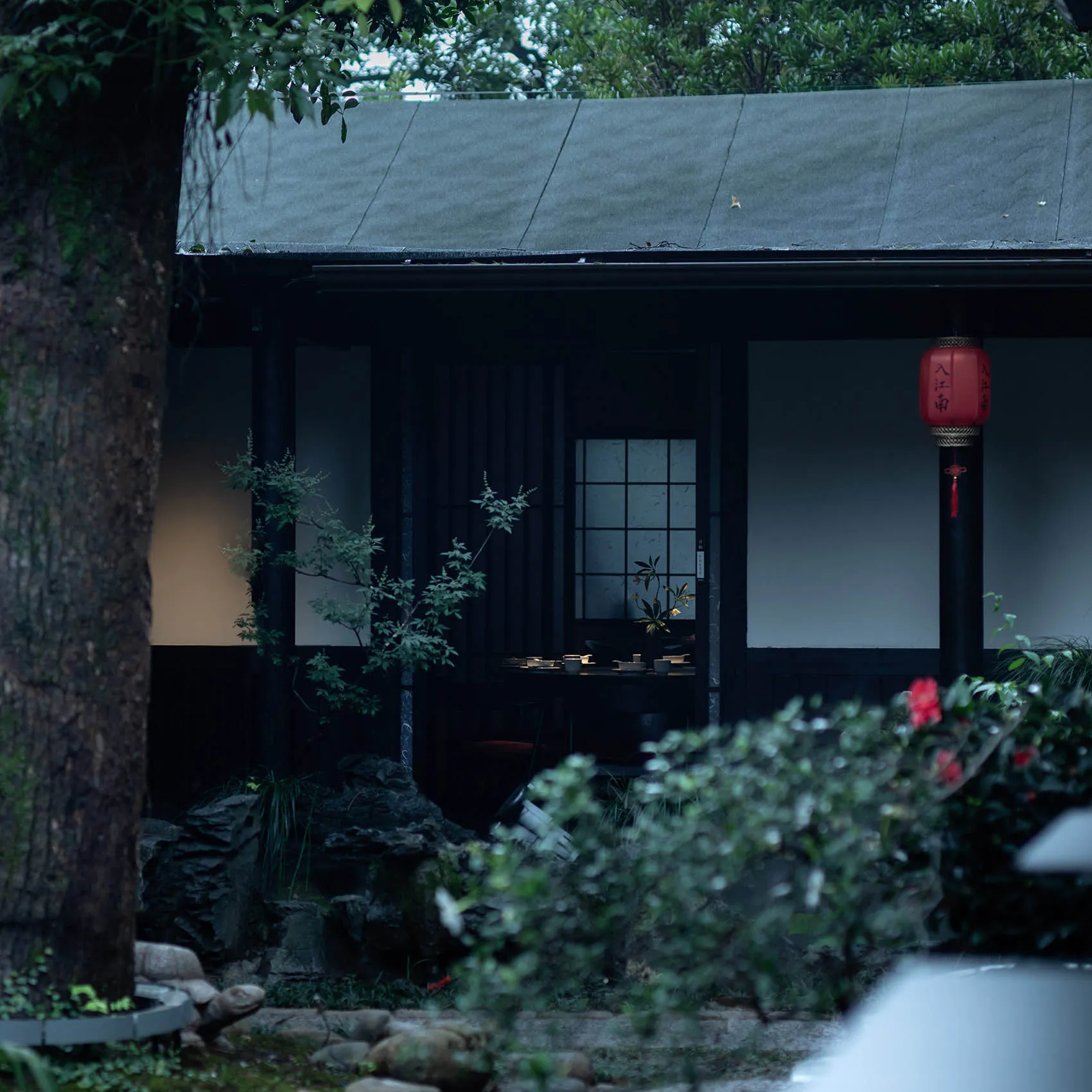 亞洲風格住宅，外牆為黑色，周圍環繞綠意，庭園區設有石牆及門口盆栽，營造寧靜祥和氛圍