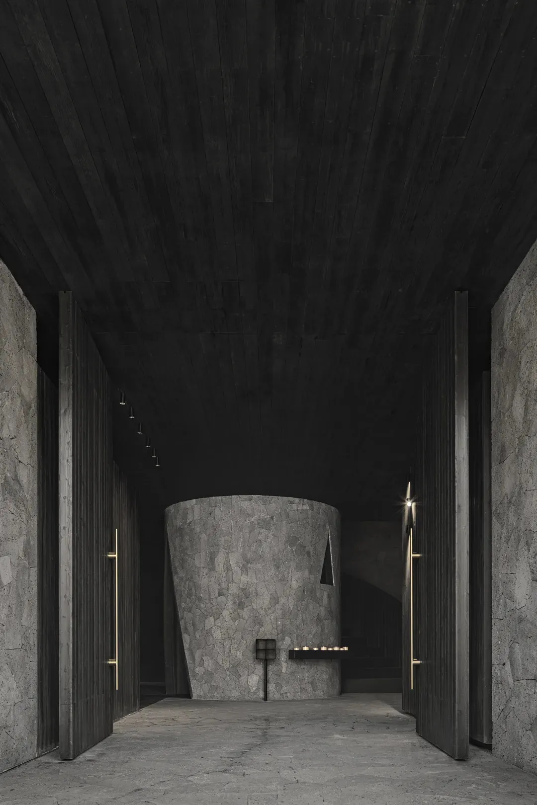 Dark empty room with a stone wall and a wooden door, lit by two lights on either side