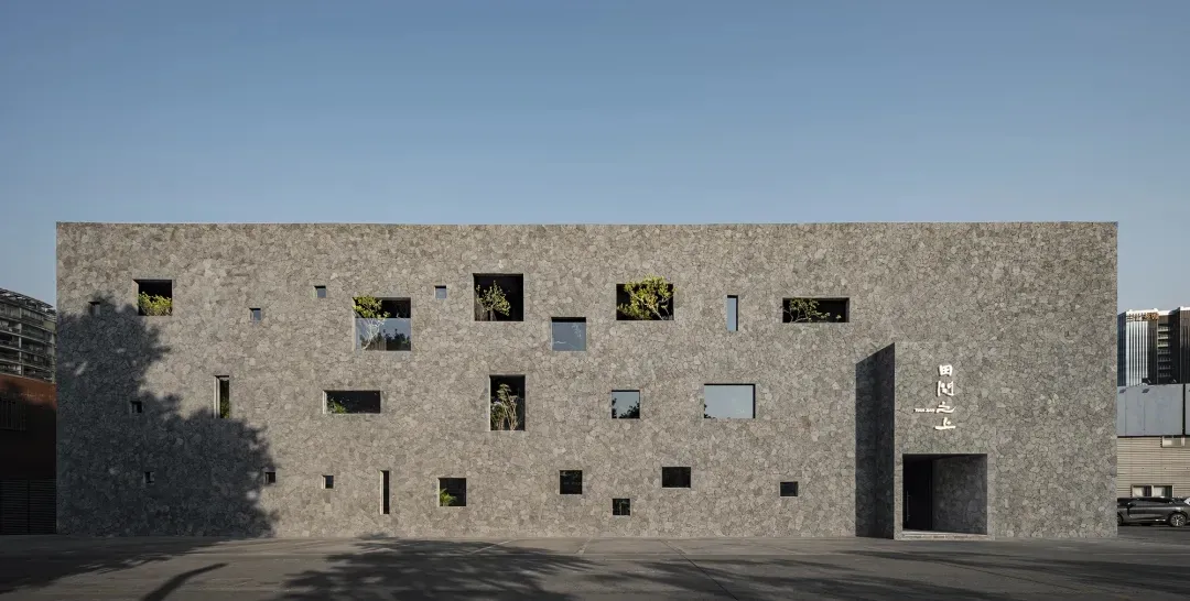 A modern building with a stone exterior, featuring multiple windows in various shapes and sizes, creating a diverse appearance