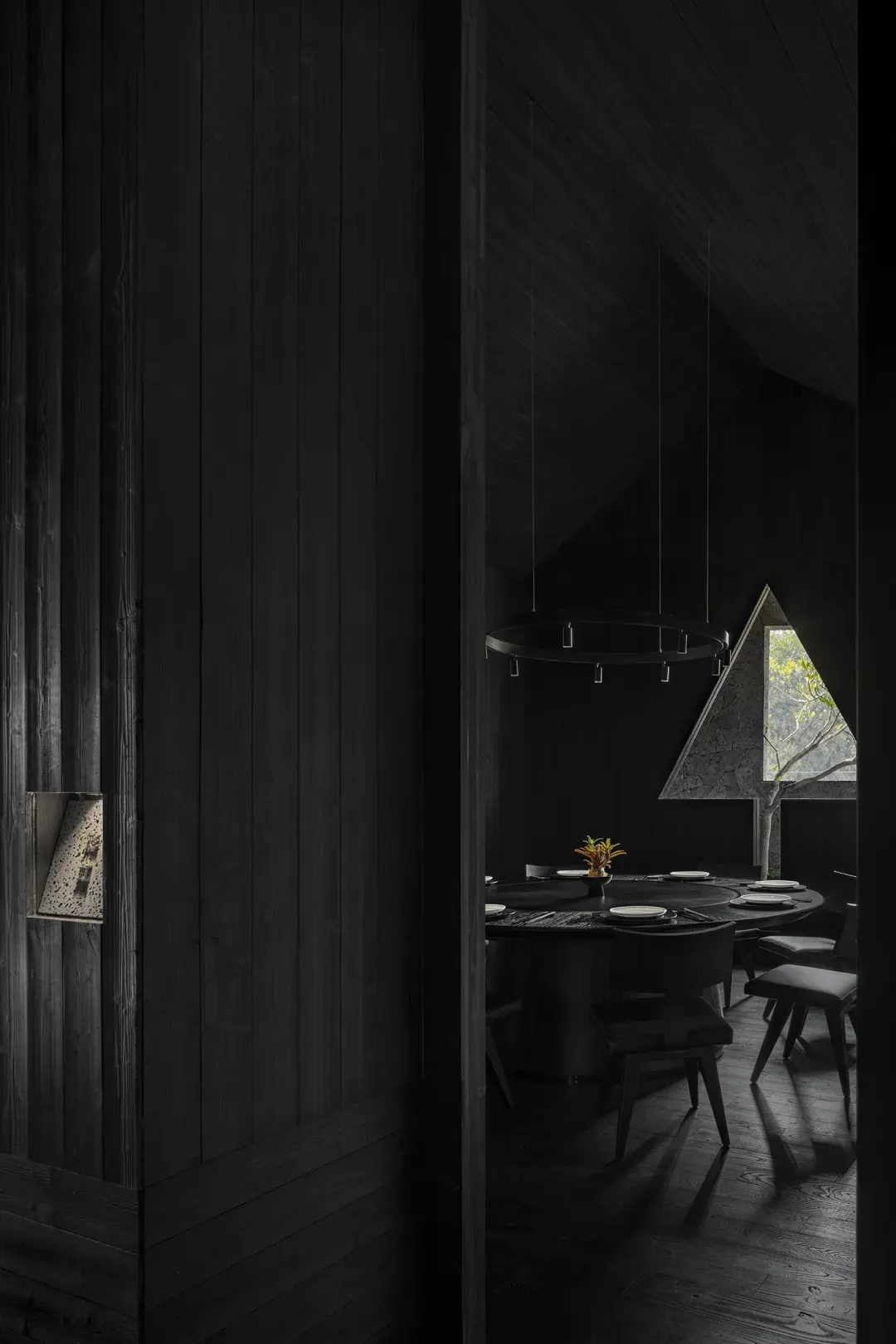 A dimly lit dining area with a large wooden table, metal chairs, and a vase, creating a cozy atmosphere