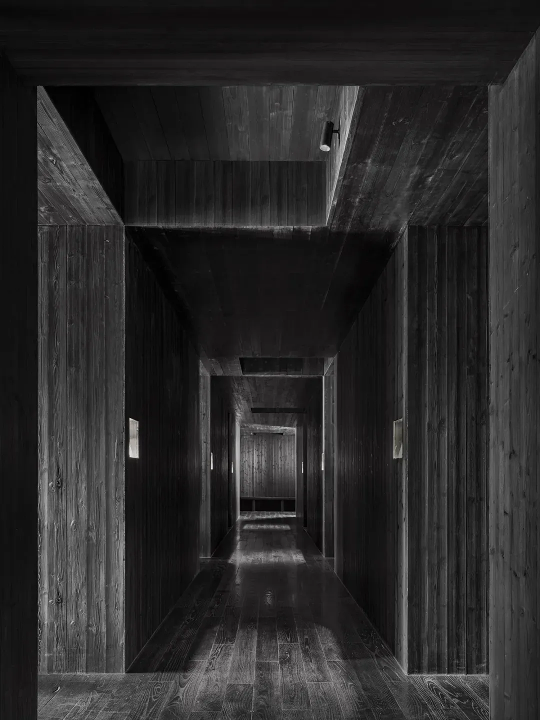 A dark and empty hallway with a wooden floor, devoid of people or objects, creating a sense of mystery