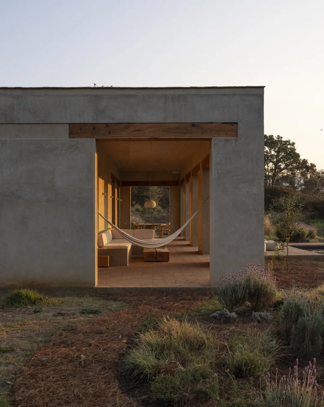 A relaxed outdoor living space with a hammock as the centerpiece, surrounded by chairs and a dining table, set in a natural environment
