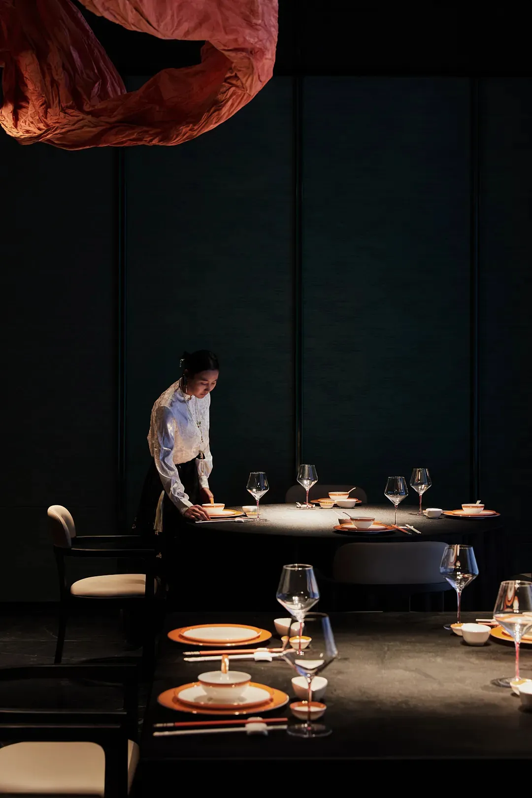 A woman stands in front of a dining table set up with wine glasses, bowls, and cups, creating an elegant and inviting atmosphere