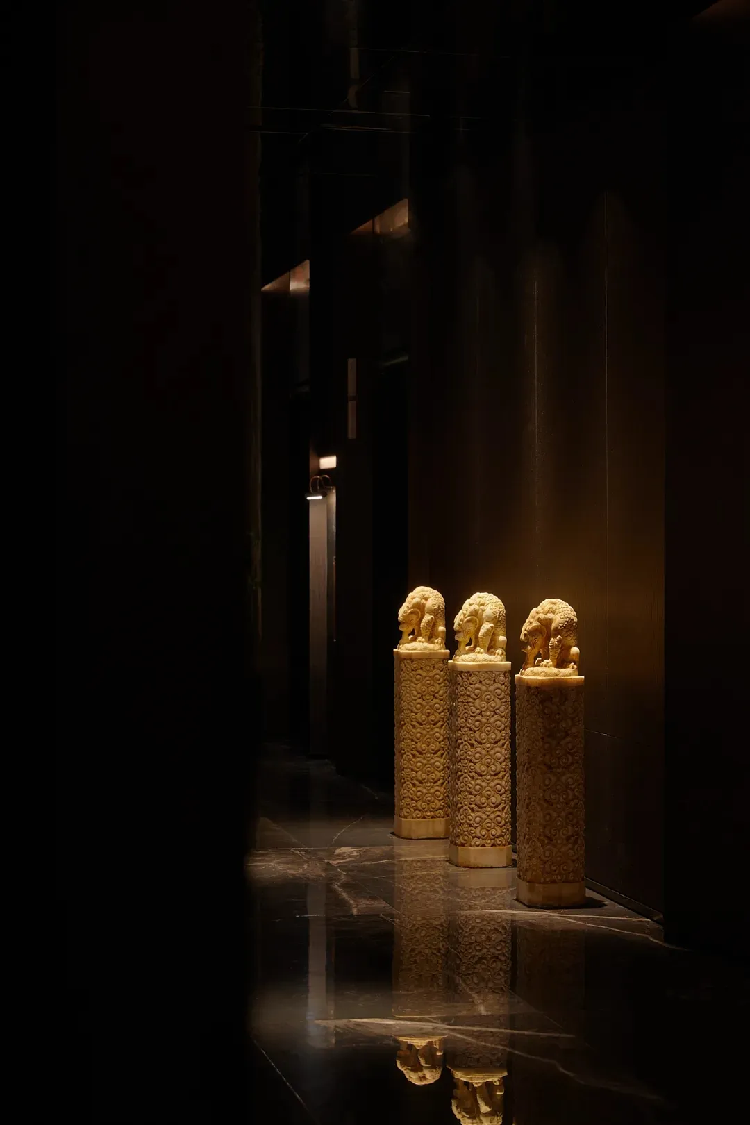 A sophisticated hallway with three golden statues on pedestals, creating a luxurious focal point