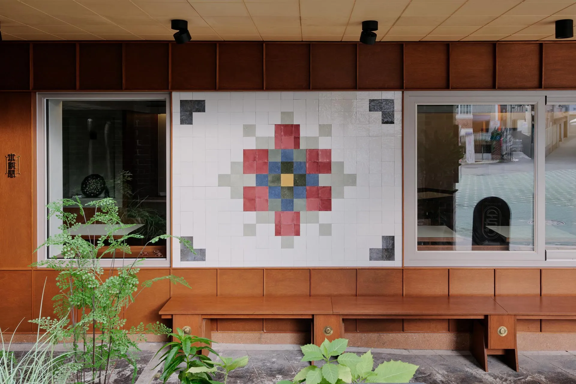 Decorative interior space with a large mosaic tile wall resembling a flower pattern, featuring two benches and three chairs