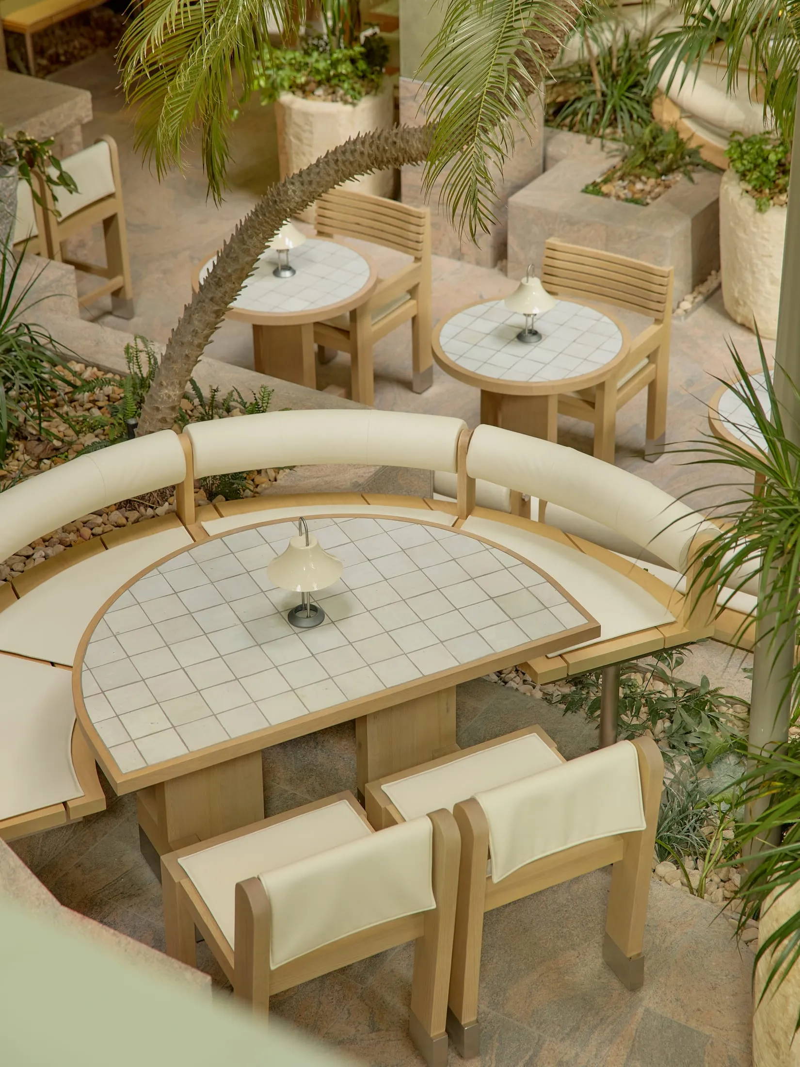 A warm and inviting outdoor dining area with wooden tables and chairs, surrounded by potted plants and a comfortable seating arrangement