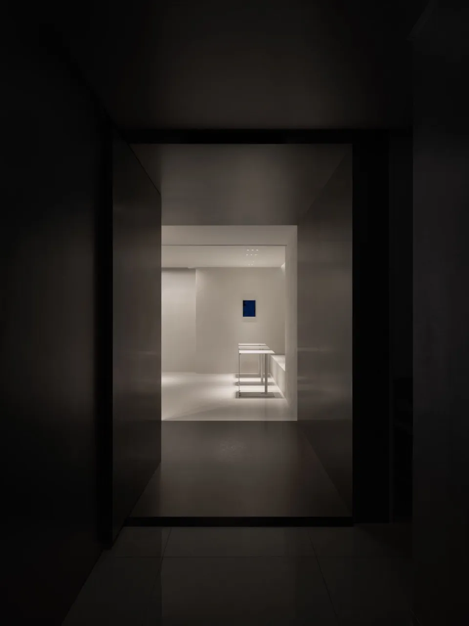 Dark hotel hallway with a black doorway, two tables, and a chair, lacking natural light