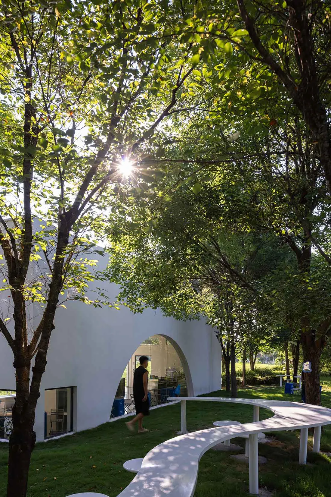 A serene scene of a modern building with a large window, surrounded by trees, and a person standing nearby, conveying a sense of tranquility and appreciation for nature and architecture
