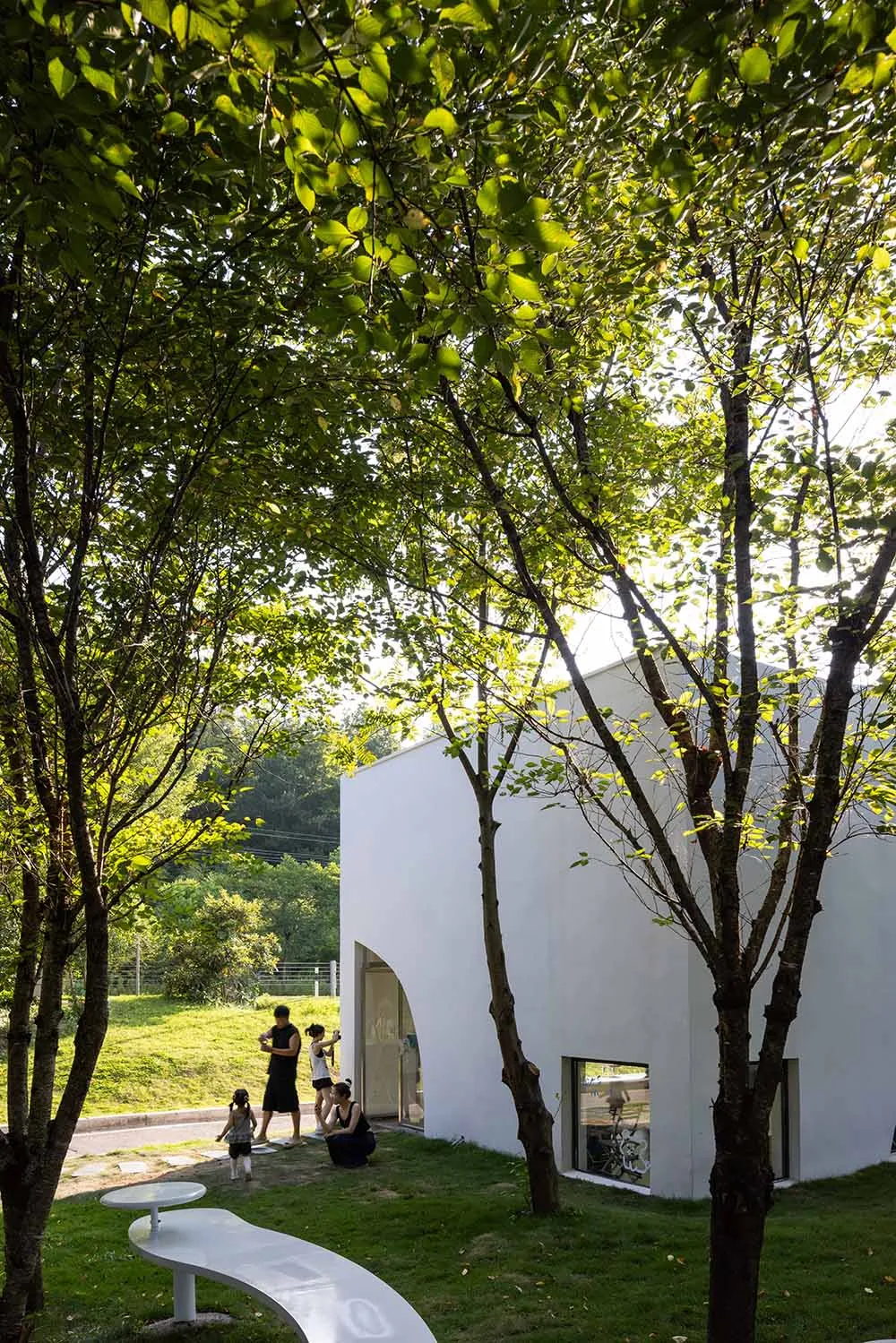 A modern building with a white facade surrounded by trees and several people standing outside, admiring its design or attending an event