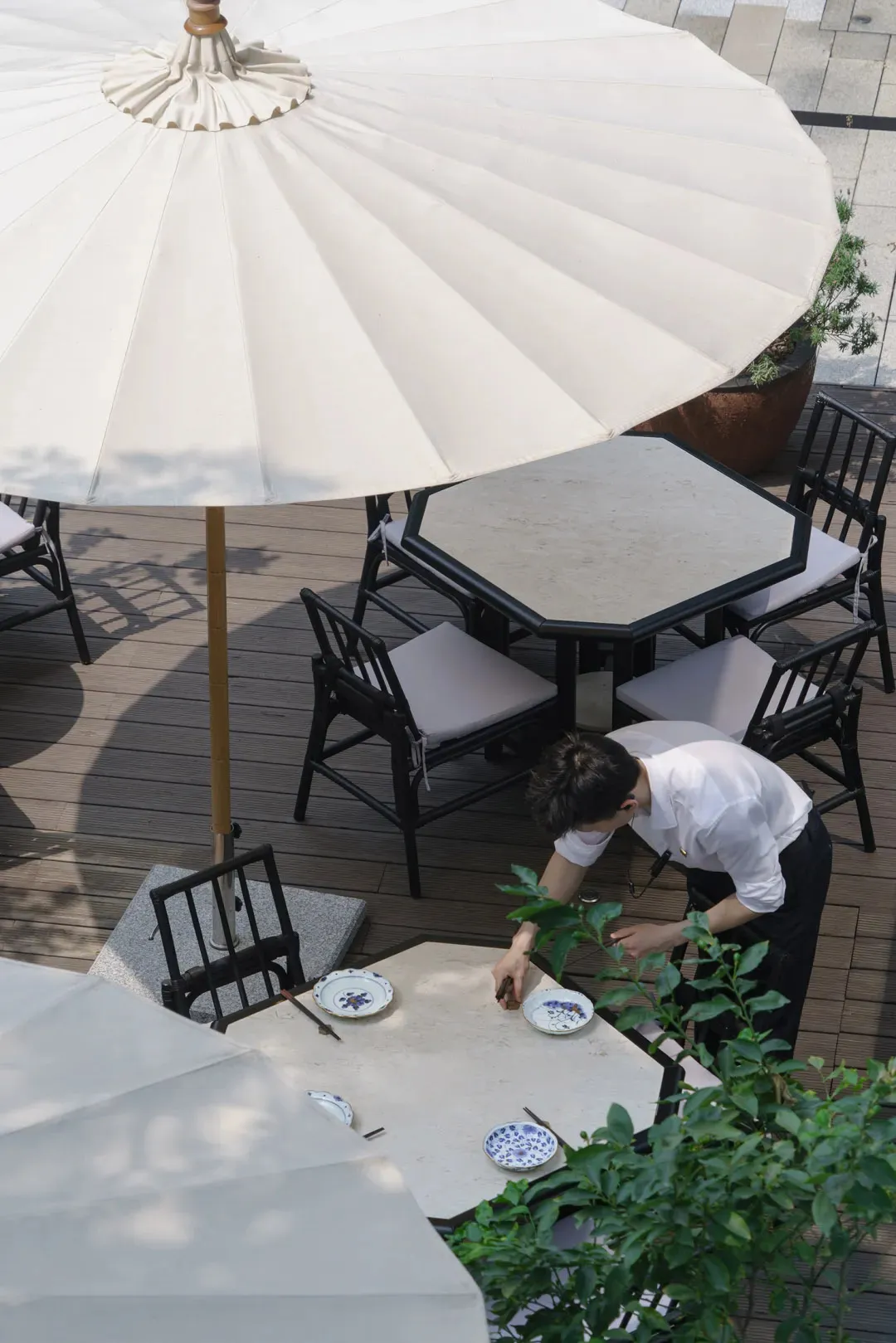An outdoor dining area with several tables and chairs under large umbrellas, featuring white tablecloths and a clean elegant atmosphere