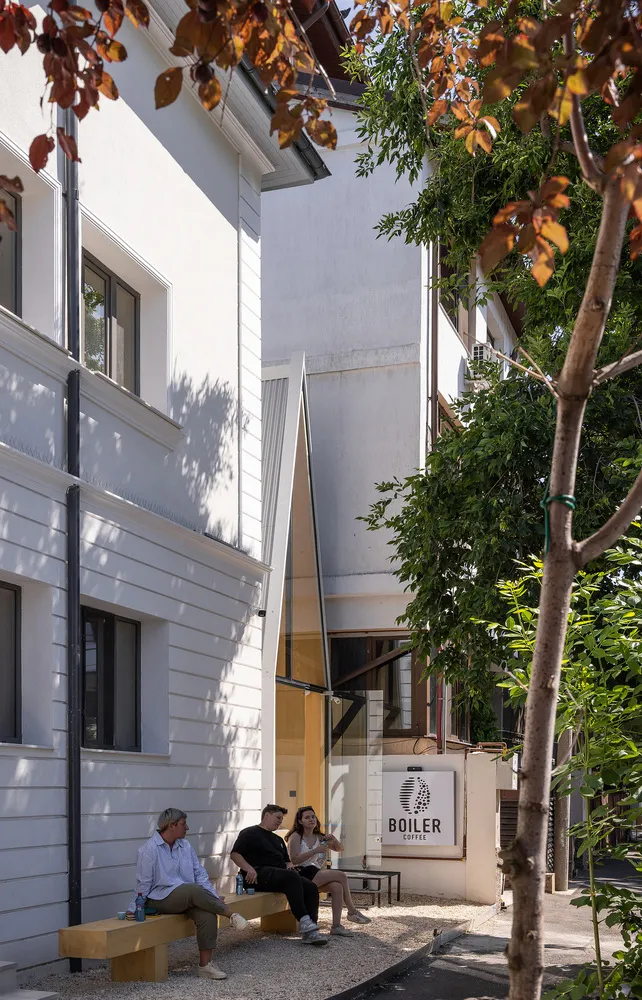 A modern building with a glass door and balcony, featuring white walls and a wooden door, with three people standing in front, admiring the view or waiting to enter