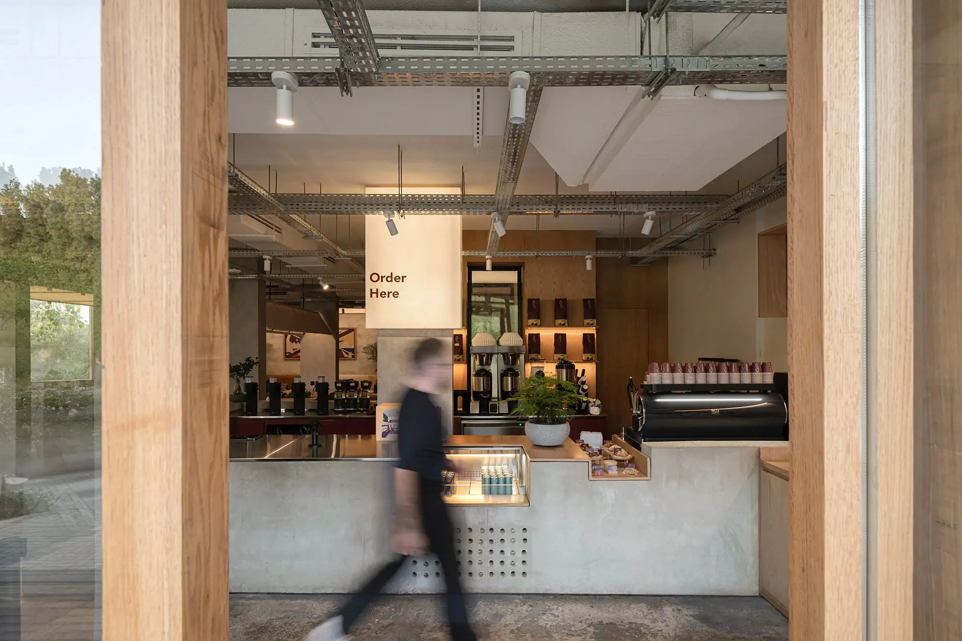 A modern coffee shop interior with a concrete floor, wooden elements, and a casual atmosphere, featuring a man walking past the counter