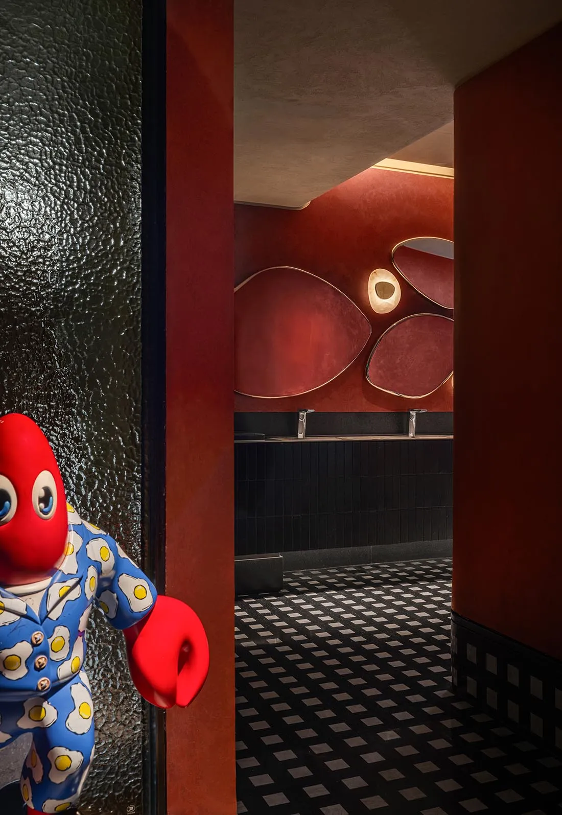 A plush red crab stands in a doorway of a restaurant with a black and white checkered floor