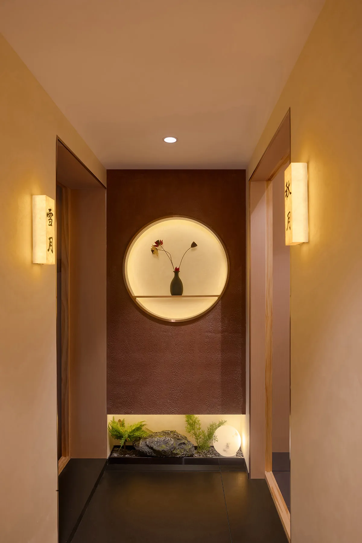 A warm and inviting hallway with a brown wall, a mirror, a vase of flowers, and two lights providing illumination
