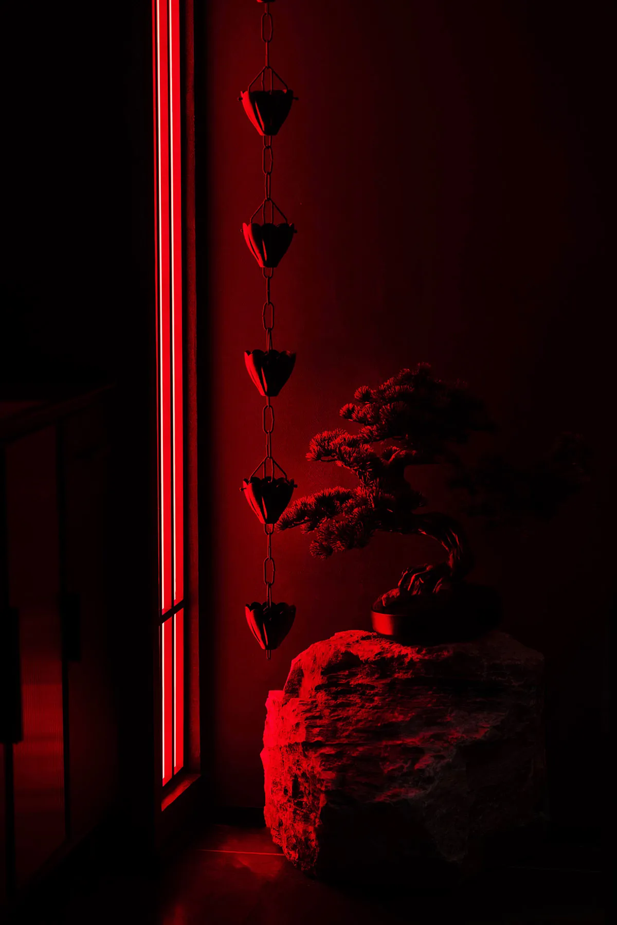 A small bonsai tree sits on a rock in front of a red wall, surrounded by heart-shaped decorations in a cozy indoor space