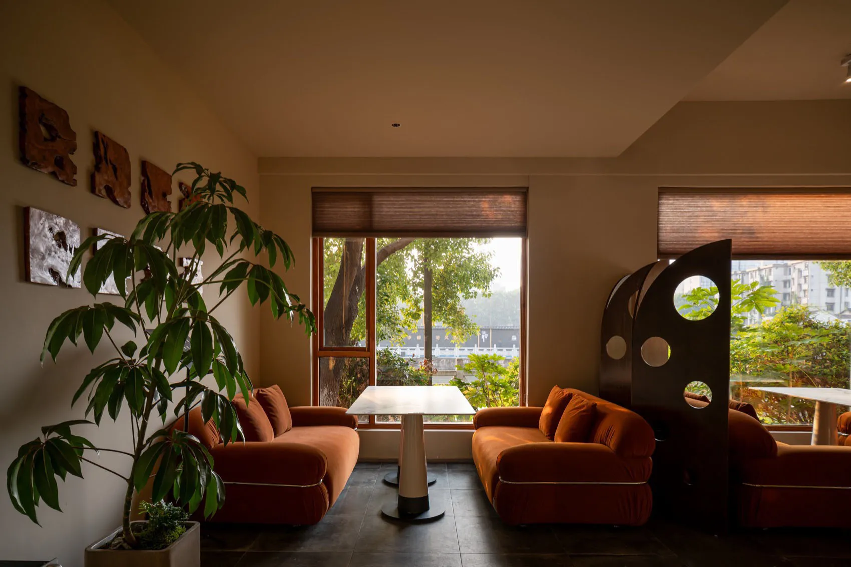 Modern living room with two orange couches in front of large windows, surrounded by a white wall, wooden floors, and potted plants