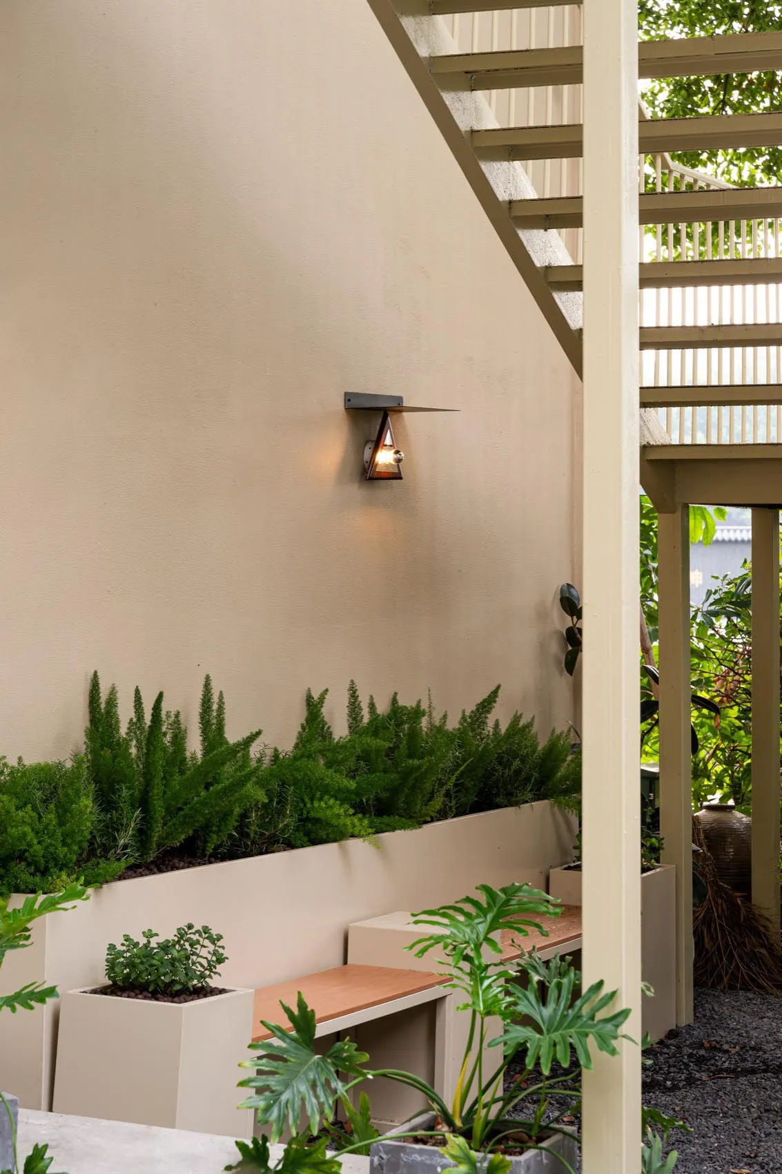 A wooden deck with a bench seating arrangement surrounded by potted plants and a bird, set in a relaxing outdoor space with a focus on greenery and natural elements