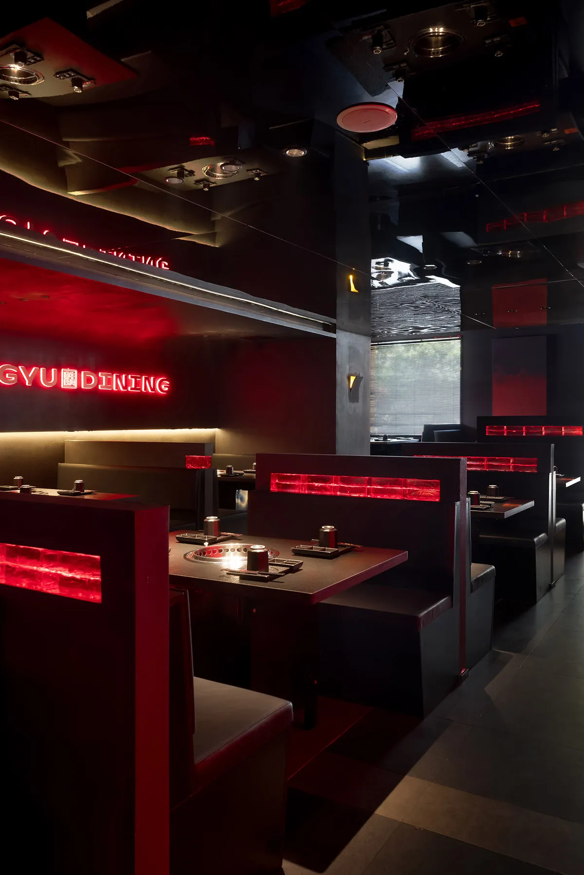 Empty modern restaurant interior with black walls, red accents on tables, and dining tables and chairs throughout