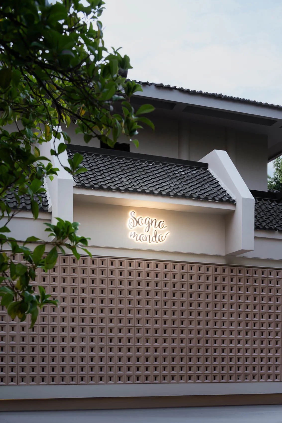 現代建築擁有白色混凝土立面、瓦片屋頂，以及多扇配有百葉窗的窗戶，背景寧靜祥和