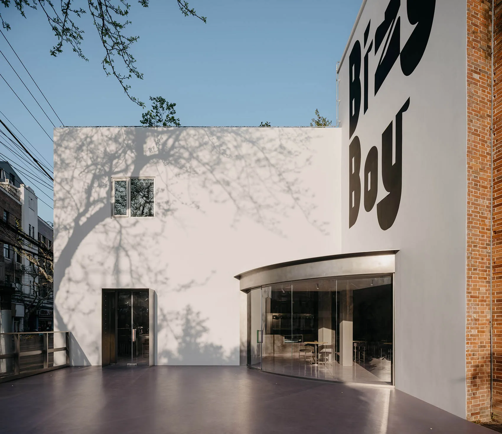 A modern building with a concrete exterior, featuring a large white wall with black lettering, surrounded by outdoor seating and a dining table