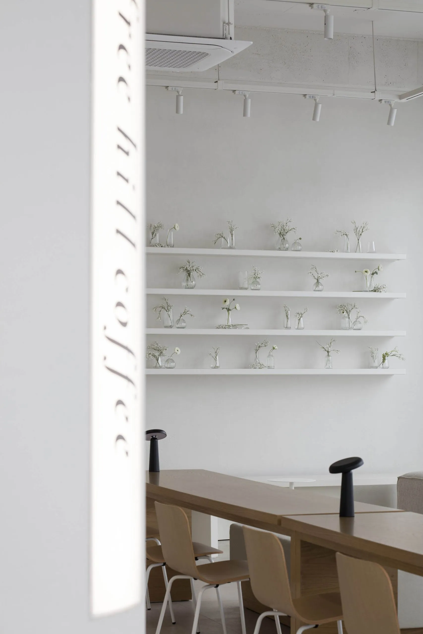 A coffee shop showroom with white walls, multiple tables, chairs, and decorative vases, creating a cozy atmosphere