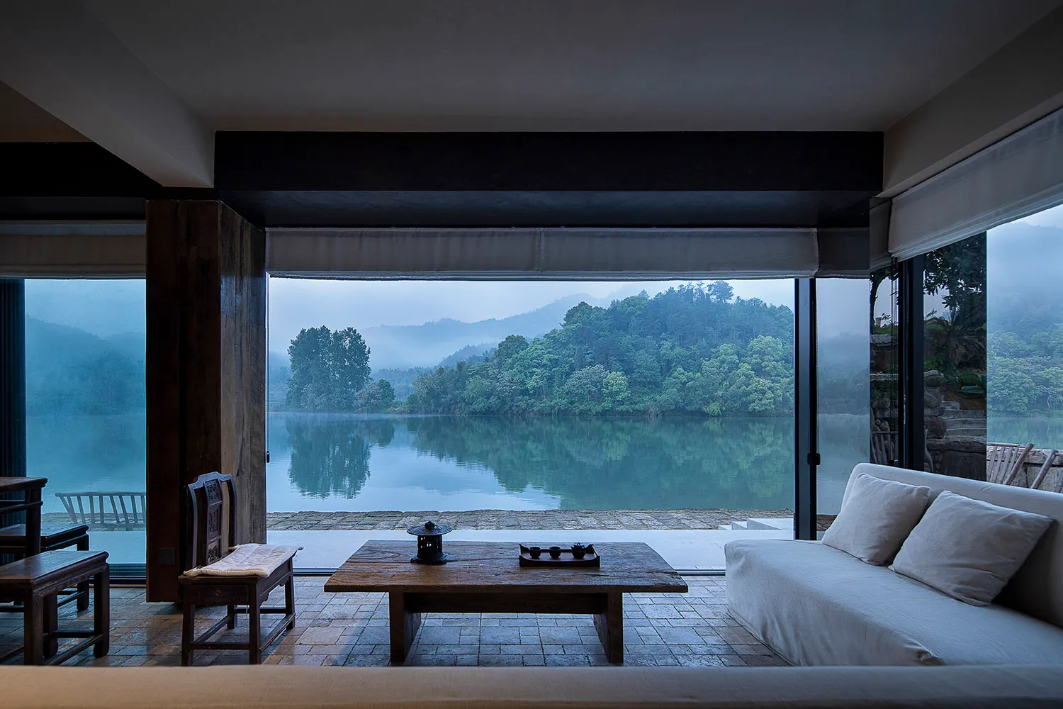 Cozy indoor living area with a large window overlooking a lake, featuring two couches, a dining table, and chairs, with a focus on relaxation and enjoying the view outside