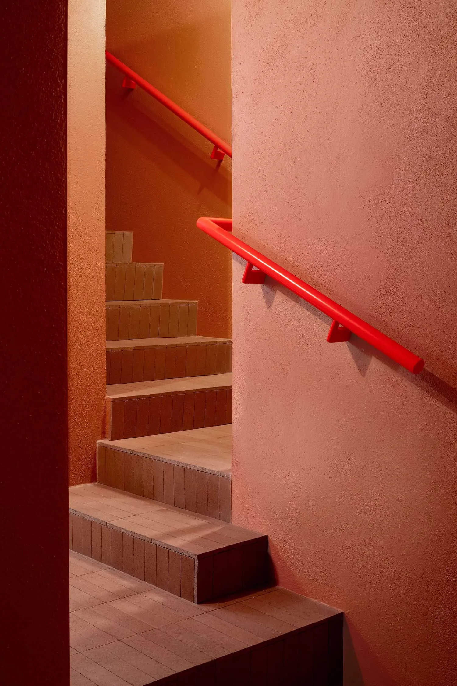 Orange hallway with red handrails, concrete walls, and a staircase leading upwards