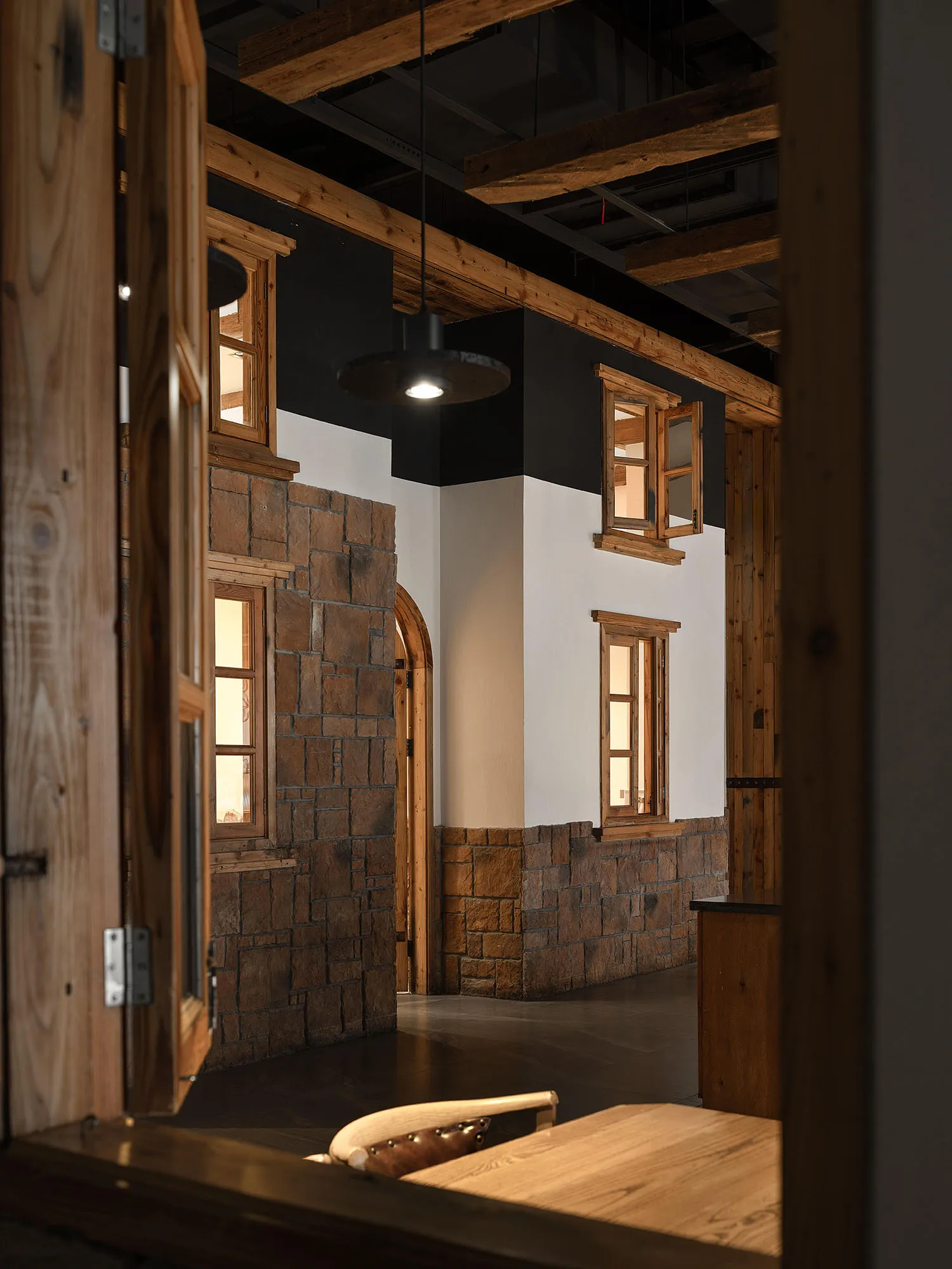Interior of a historic building with a large stone wall, wooden floors, and two windows, giving a sense of a cultural site