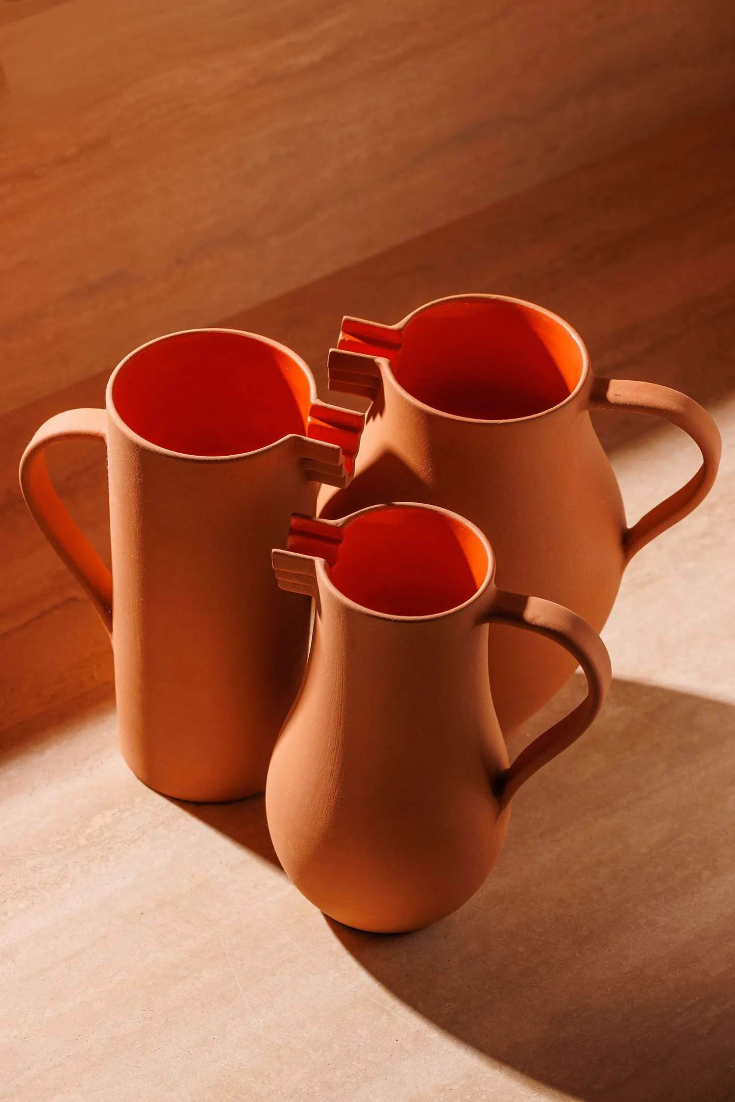 Three stacked brown ceramic pitchers with orange handles sit on a wooden table, adding a pop of color to the space