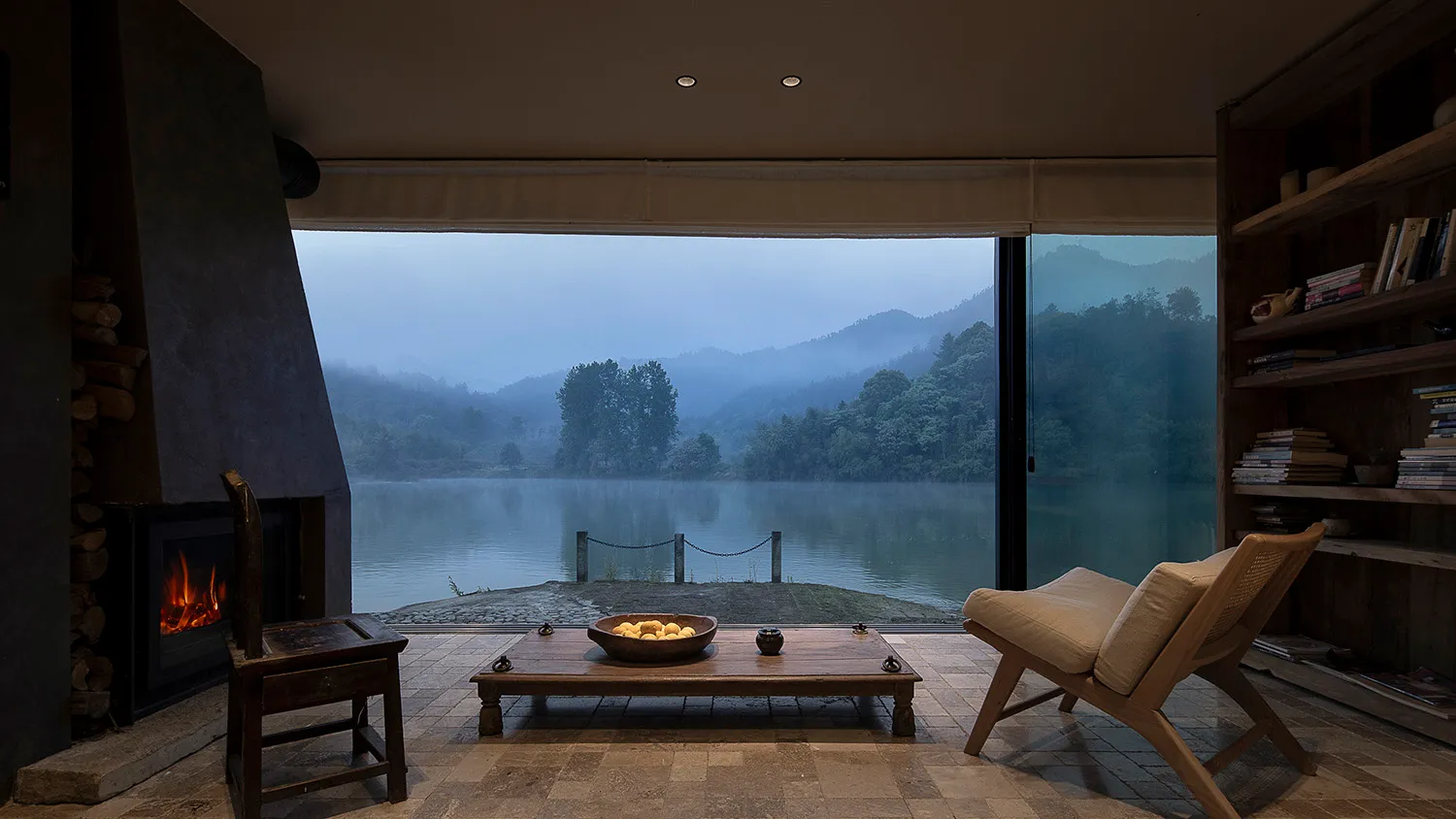 Cozy living area with a wooden table, chairs, and couch, overlooking a lake through a large window