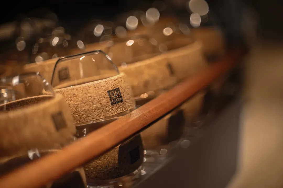 各種形狀與尺寸的酒杯置於木質置物架上，呈現泥土色調與自然質感
