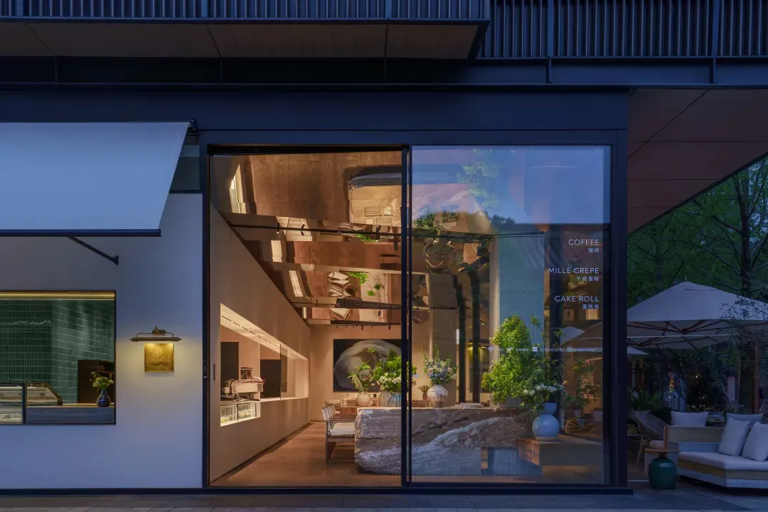 Open modern living area with glass door to patio, couches, dining table, chairs, potted plants, and TV mounted on the wall