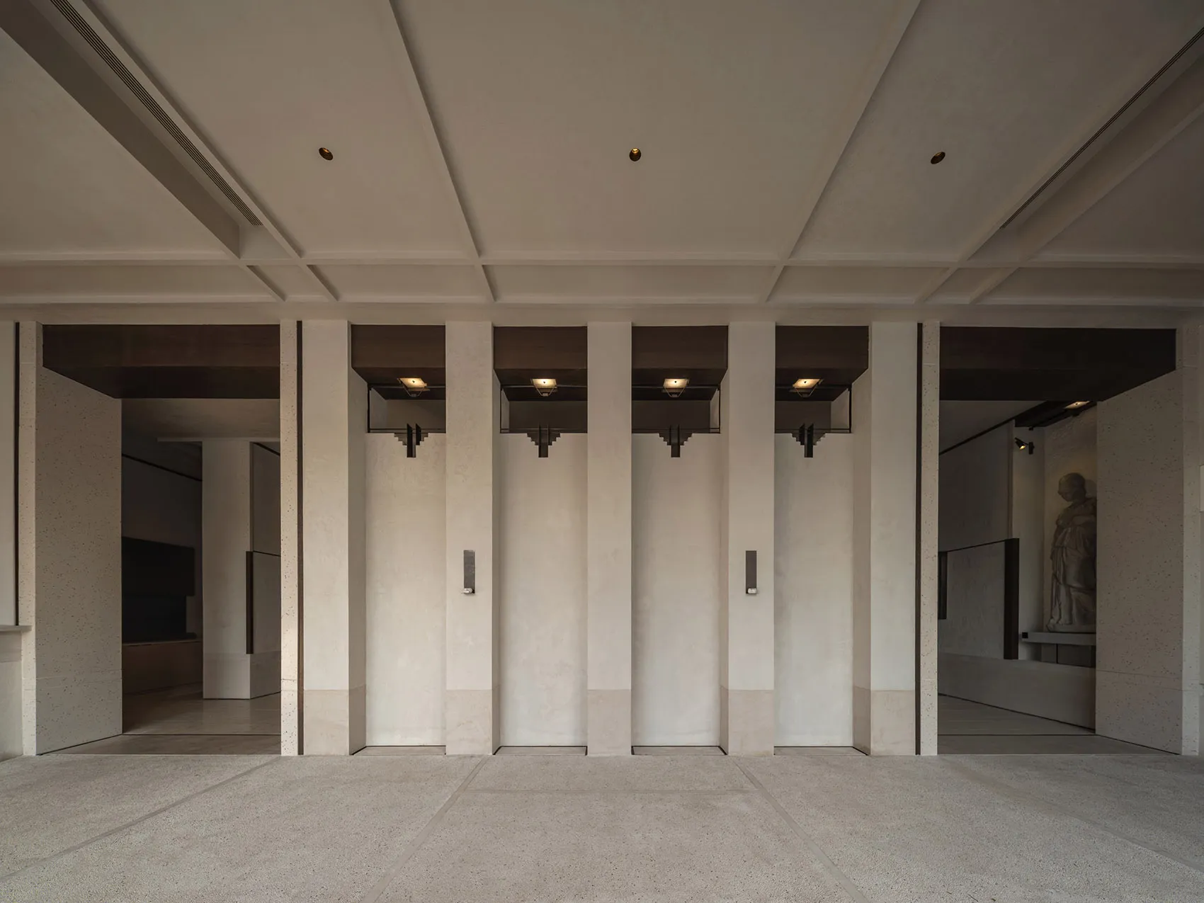 Empty hallway with concrete walls, three doors, and light fixtures above each door
