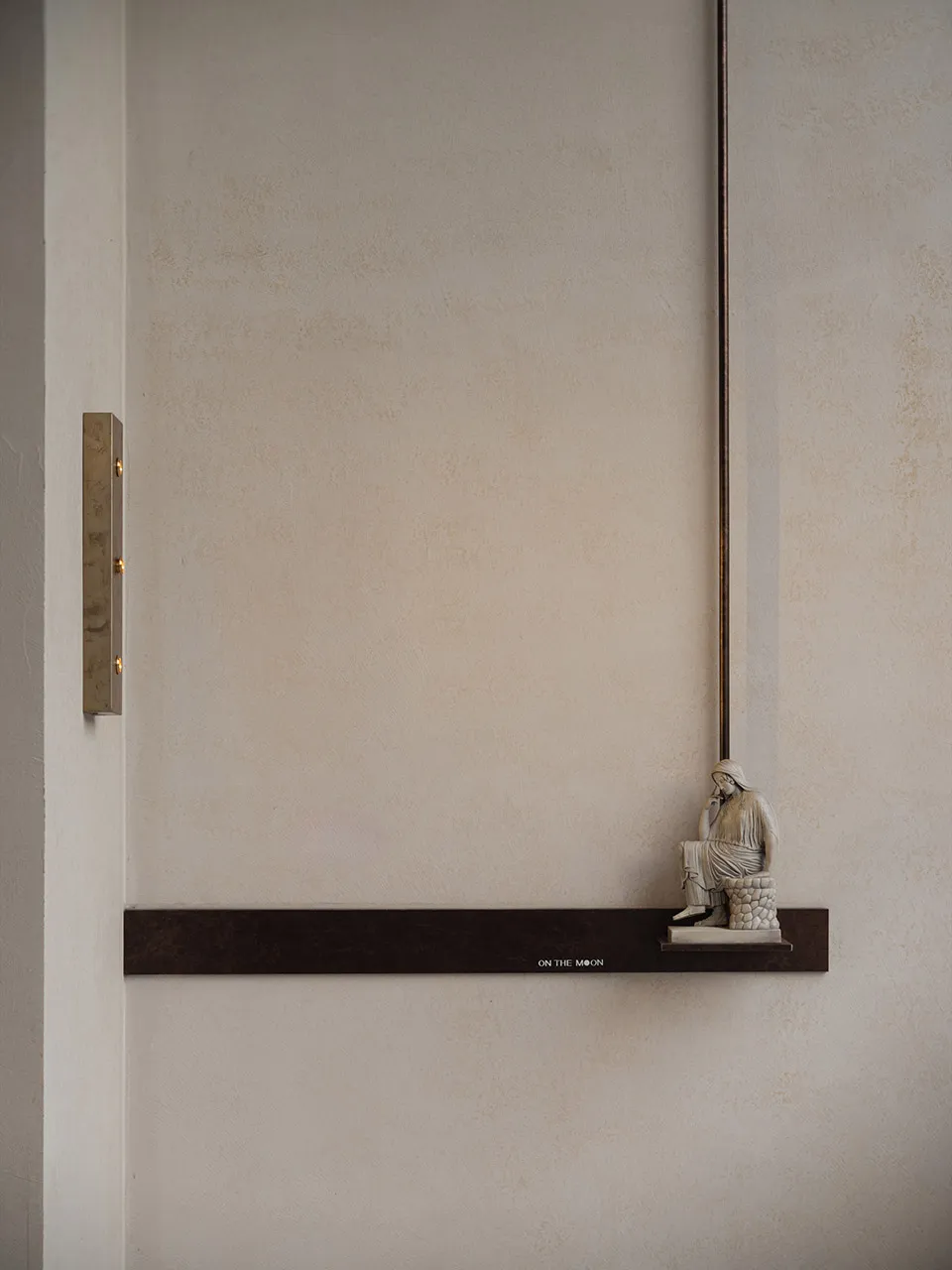 A calm and serene interior space with a concrete wall, a small statue on a ledge, and two lights, creating a peaceful atmosphere