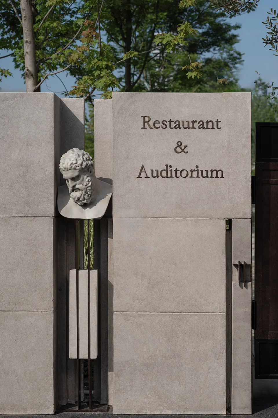 A stone wall with a marble bust of a man, a sign reading Restaurant & Auditorium, and a sophisticated interior space