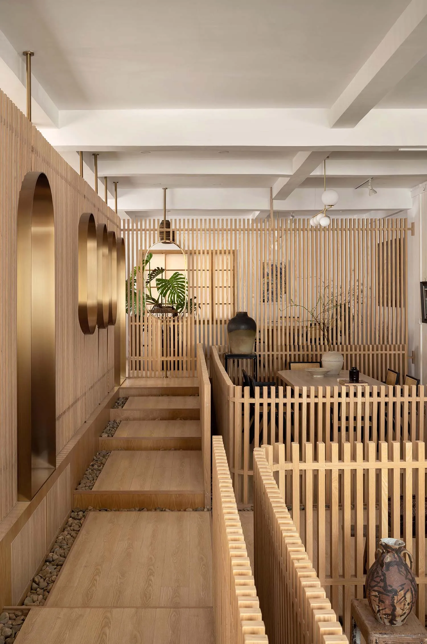 溫暖舒適的家宅內部，木質牆面與地板，包含餐廳、客廳，以及通往另一層樓的階梯，融入自然元素與盆栽