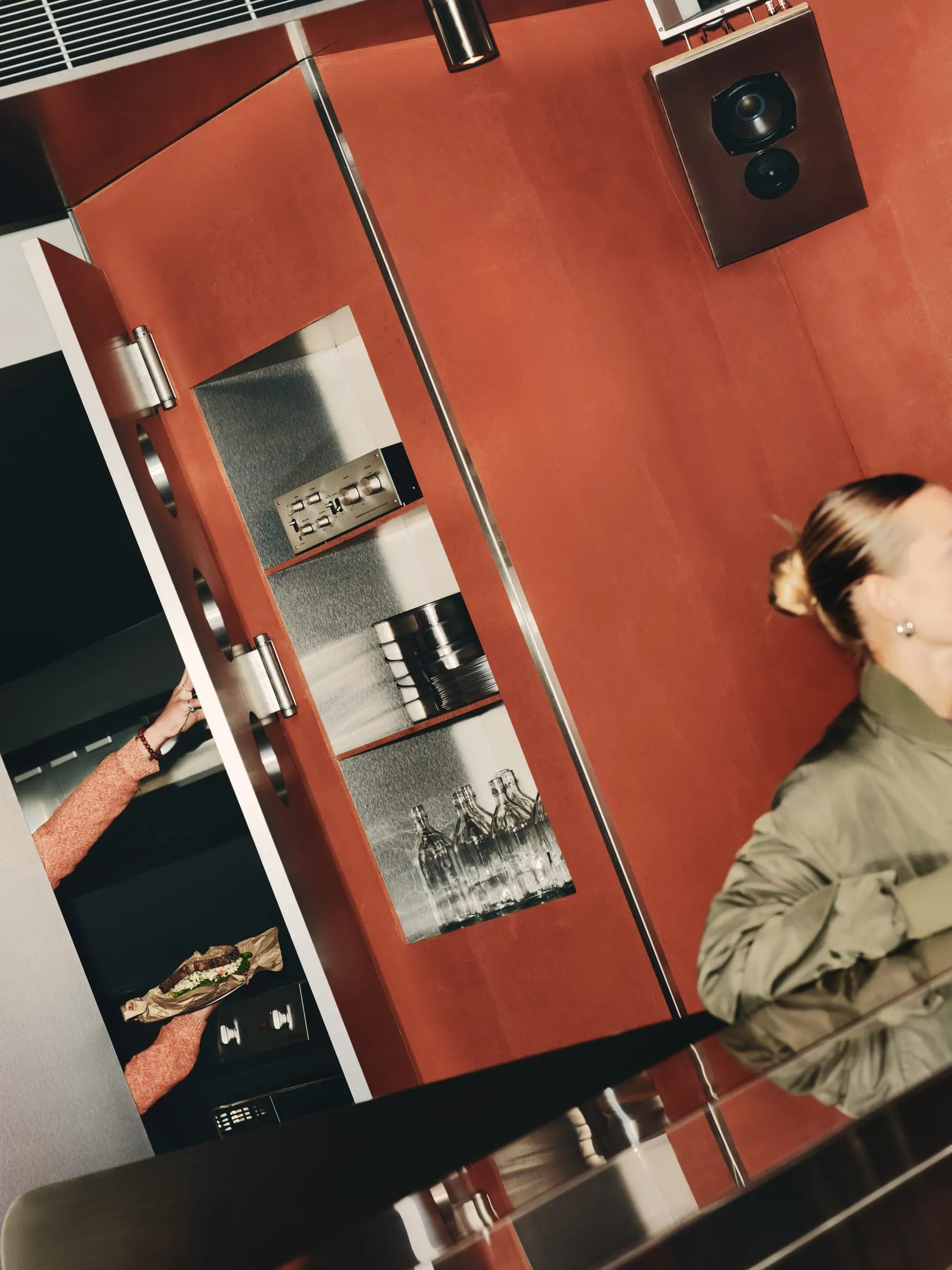 A casual kitchen scene with a woman standing in front of an open refrigerator, surrounded by wine glasses and everyday cooking items