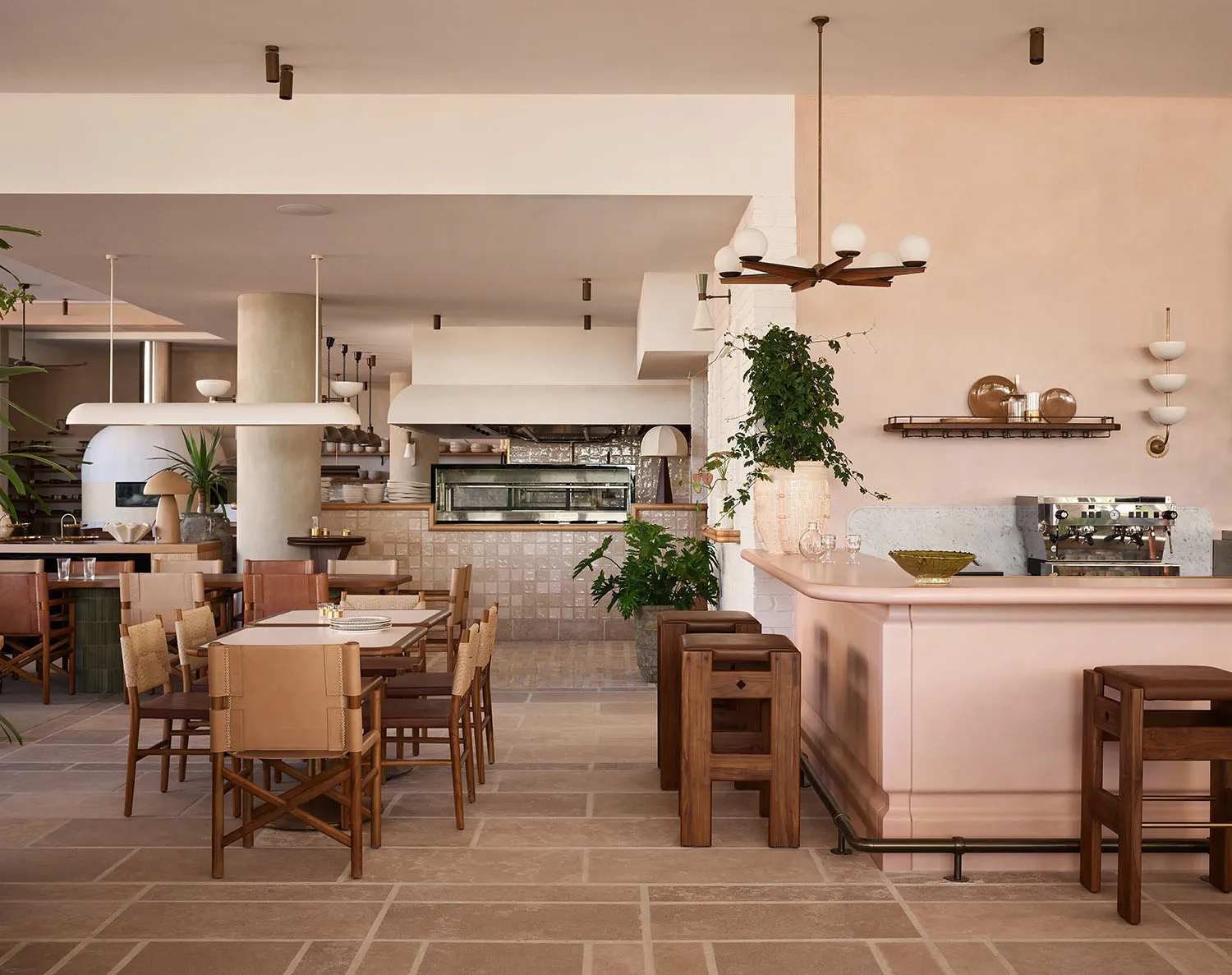 A modern restaurant with a pink bar, wooden furniture, and stone elements, featuring warm white and brown tones and overhead lighting