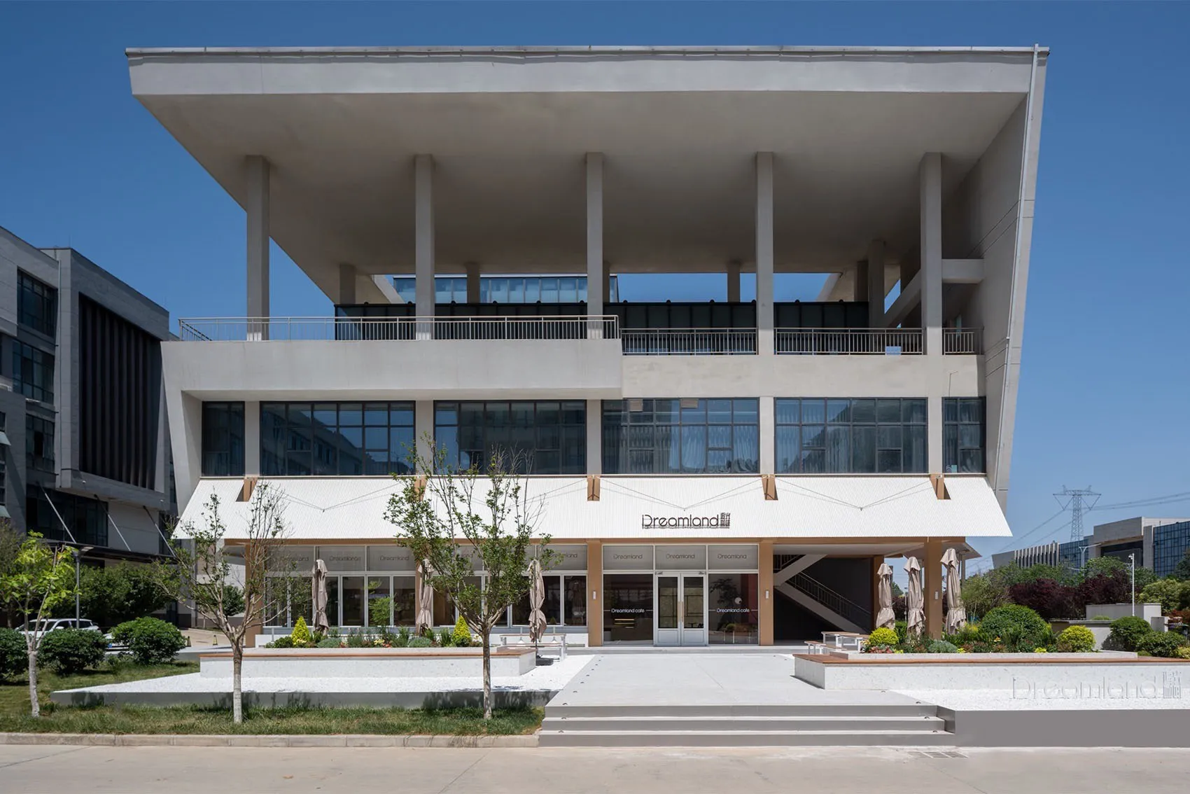 A modern building with a white exterior and green window frames, surrounded by colorful umbrellas in a outdoor setting