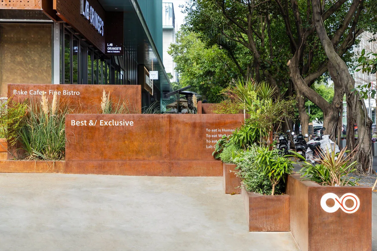 A relaxed outdoor restaurant area with potted plants, motorcycles, and scattered chairs, surrounded by a natural atmosphere