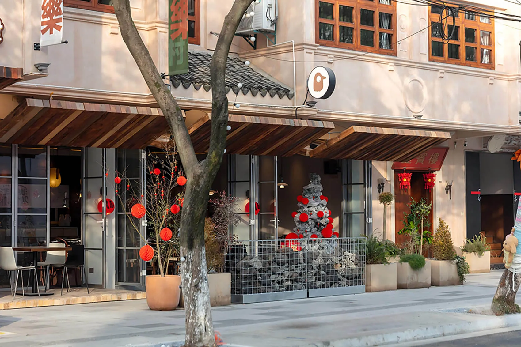 A modern Asian restaurant with a dining area, potted plants, and red lanterns outside, creating a comfortable and inviting atmosphere