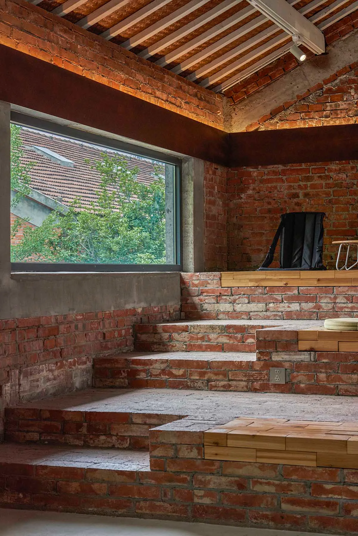 Interior of a brick building with a large window, two chairs, and a dining table, bathed in natural light